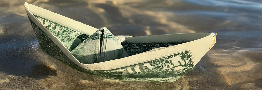 Paper boat made from a dollar bill floating in shallow water.